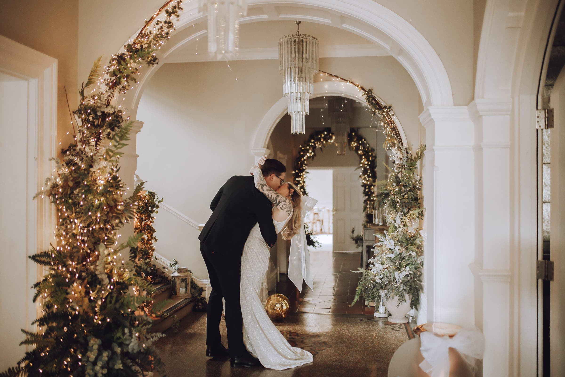 Newlyweds kissing beneath flower-lined arches, the bride wearing a long veil